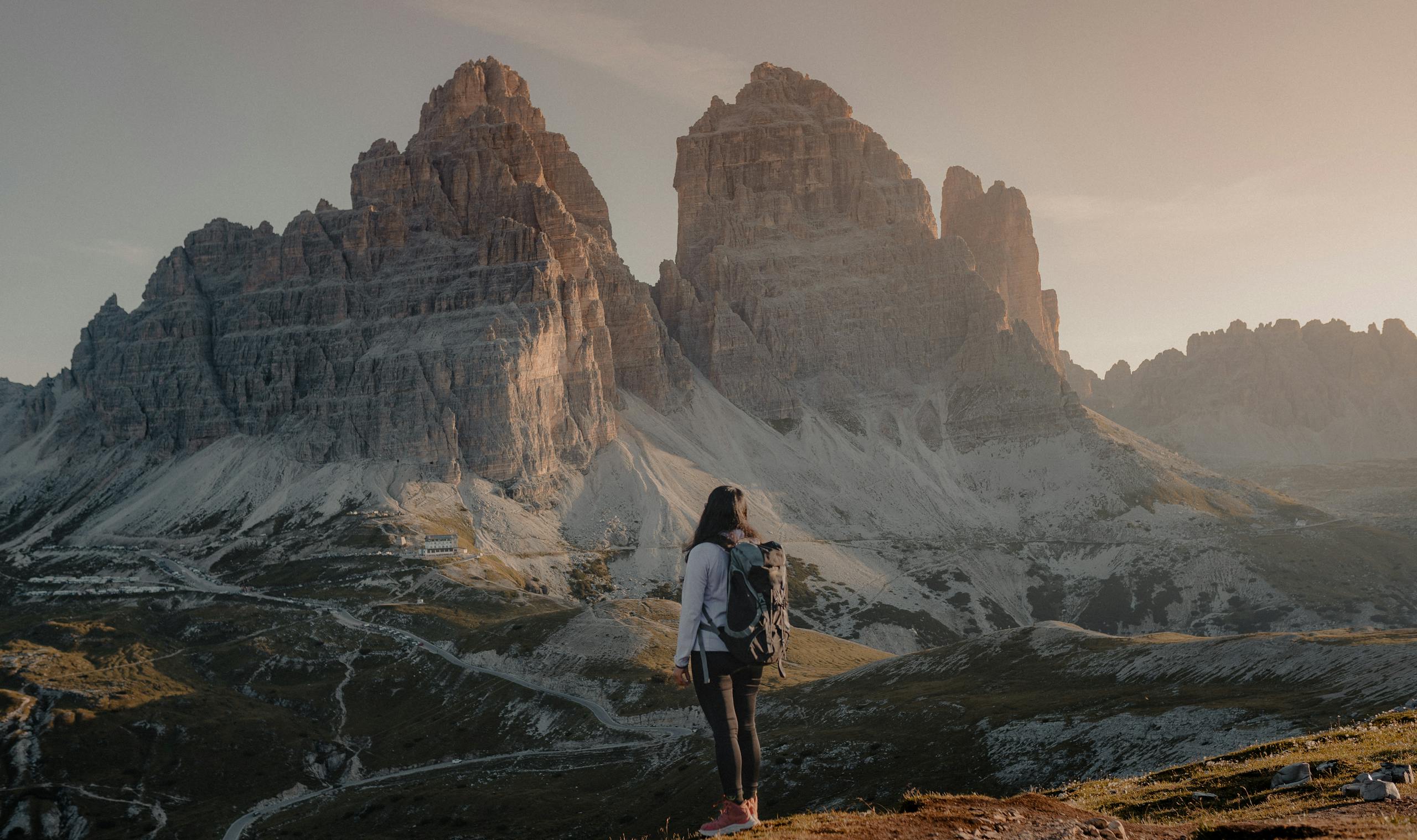 A woman hiking and admiring the stunning Tre Cime di Lavaredo during sunrise in the Dolomites.