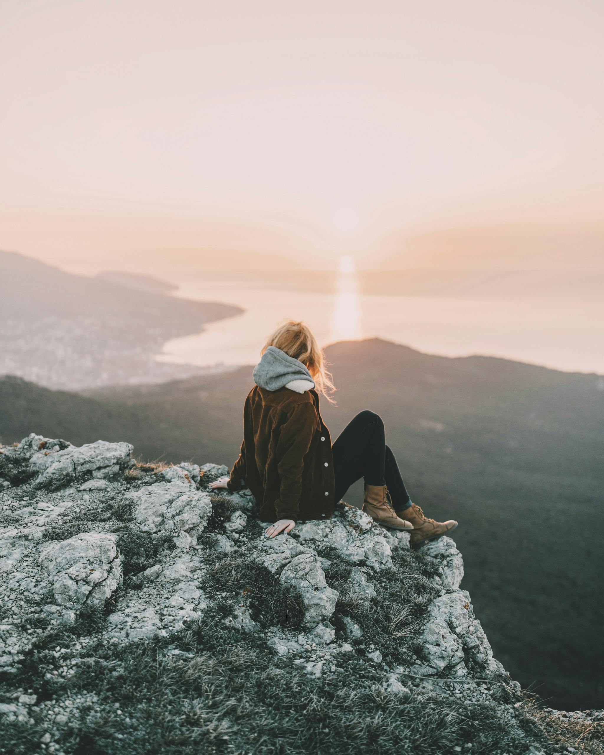 A woman sits on a rocky mountain enjoying the breathtaking sunrise view over the ocean.