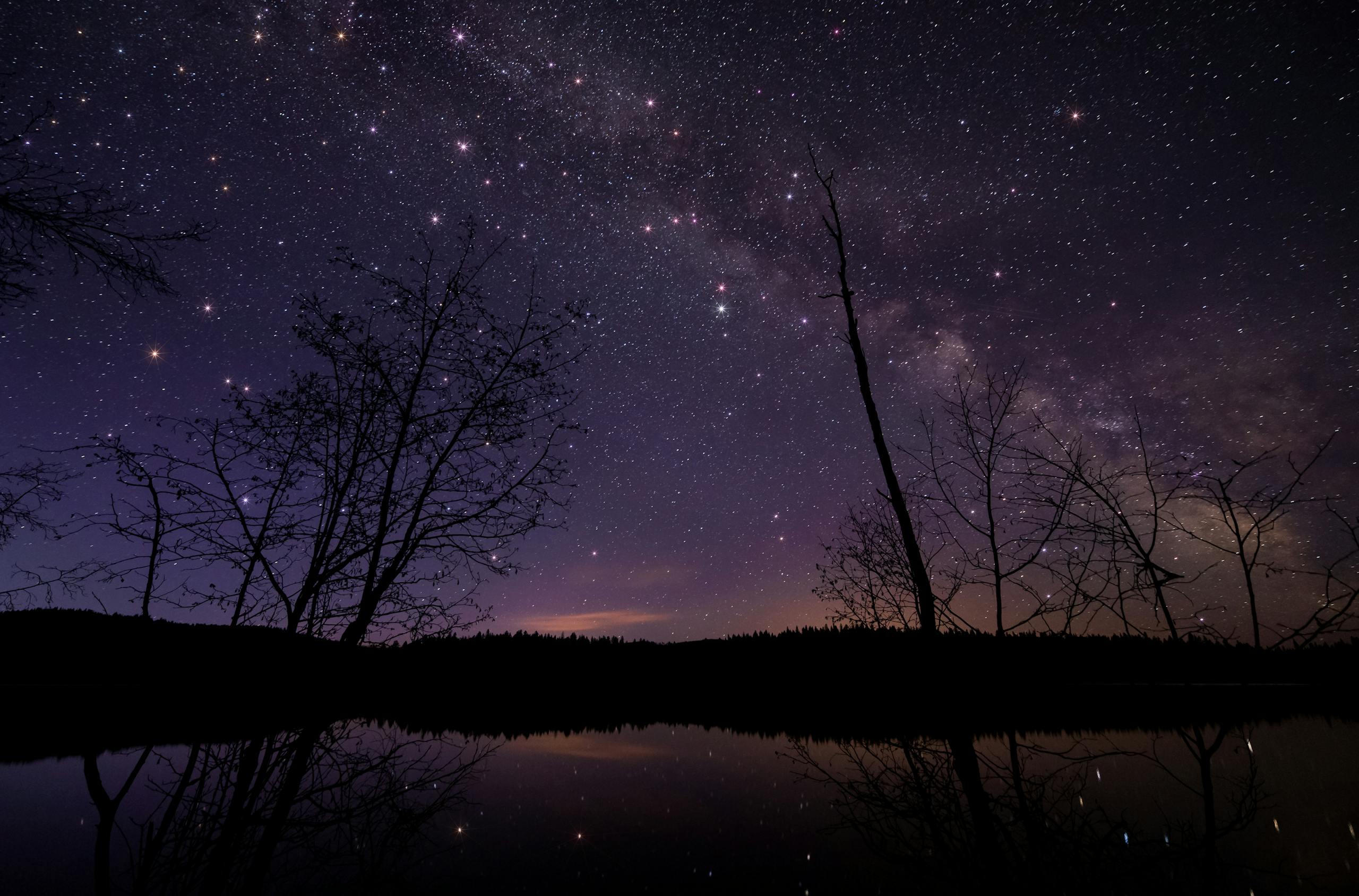 A tranquil night view of a starry sky reflecting over a calm lake.