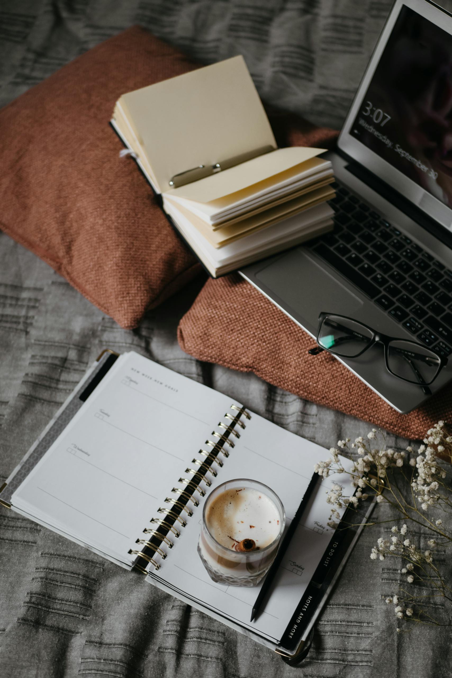 A warm, inviting home workspace featuring a notebook, laptop, and coffee on a soft surface.