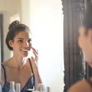 A smiling young woman enjoying her reflection in a room mirror.